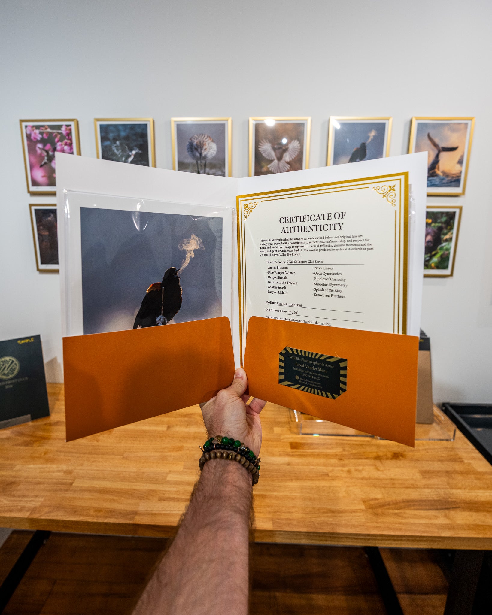 Person holding a framed photograph with a certificate of authenticity on a wooden table.